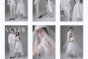 Cặp đôi nổi bật trong studio với phong cách hiện đại, cô dâu diện váy cưới trắng high-low cùng mũ và khăn voan độc đáo, chú rể lịch lãm vest trắng, tạo nên bộ ảnh cưới tối giản và sang trọng.