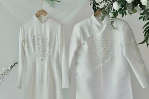 Hai bộ áo dài cưới màu trắng tinh khôi được treo trang trí cùng hoa trong studio.
