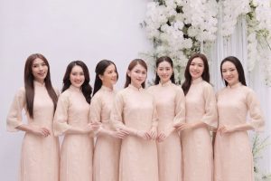 Nhóm các cô gái mặc áo dài màu hồng pastel thanh lịch trong studio với decor hoa trắng.