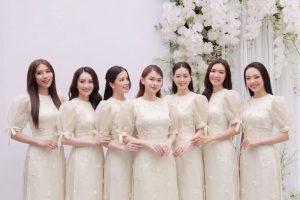 Một nhóm phụ nữ mặc áo dài trắng ngà đồng phục chụp ảnh tại studio với hoa trang trí.