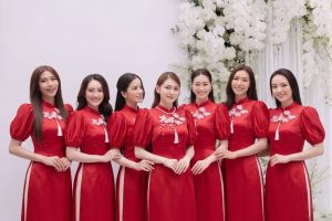Một nhóm các cô gái mặc áo dài đỏ duyên dáng chụp tại studio với hoa trắng.