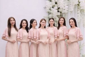 Nhóm các cô gái mặc áo dài màu hồng pastel thanh lịch trong studio với decor hoa trắng.