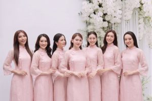 Nhóm các cô gái mặc áo dài hồng pastel chụp tại studio với hoa trắng.